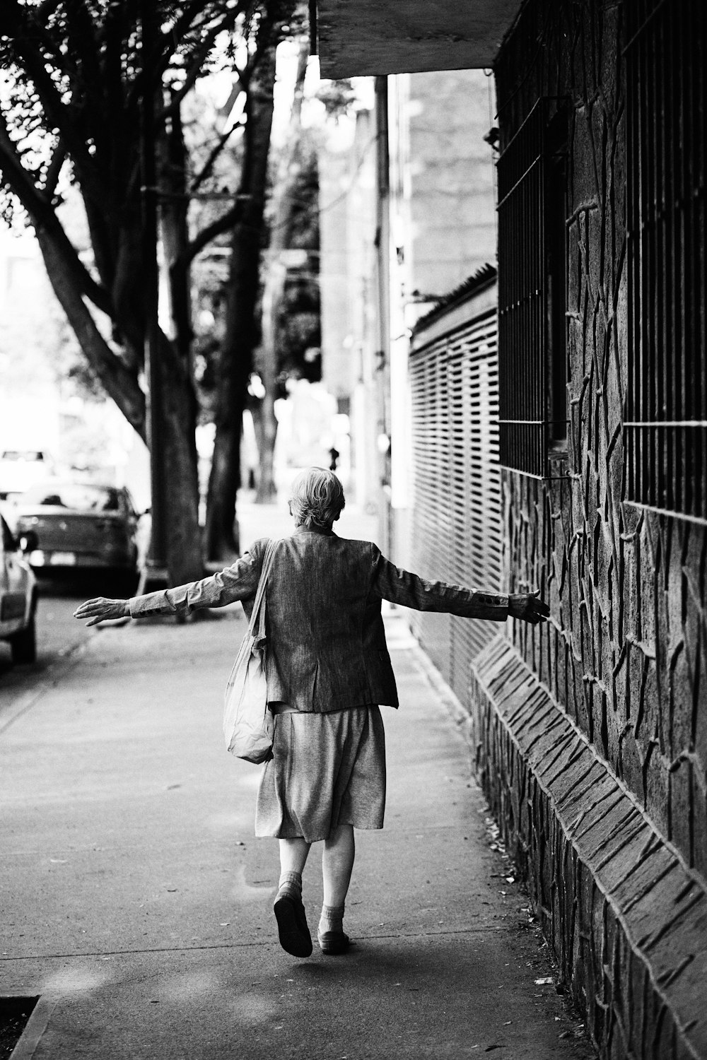 grayscale photo of woman walking on sidewalk