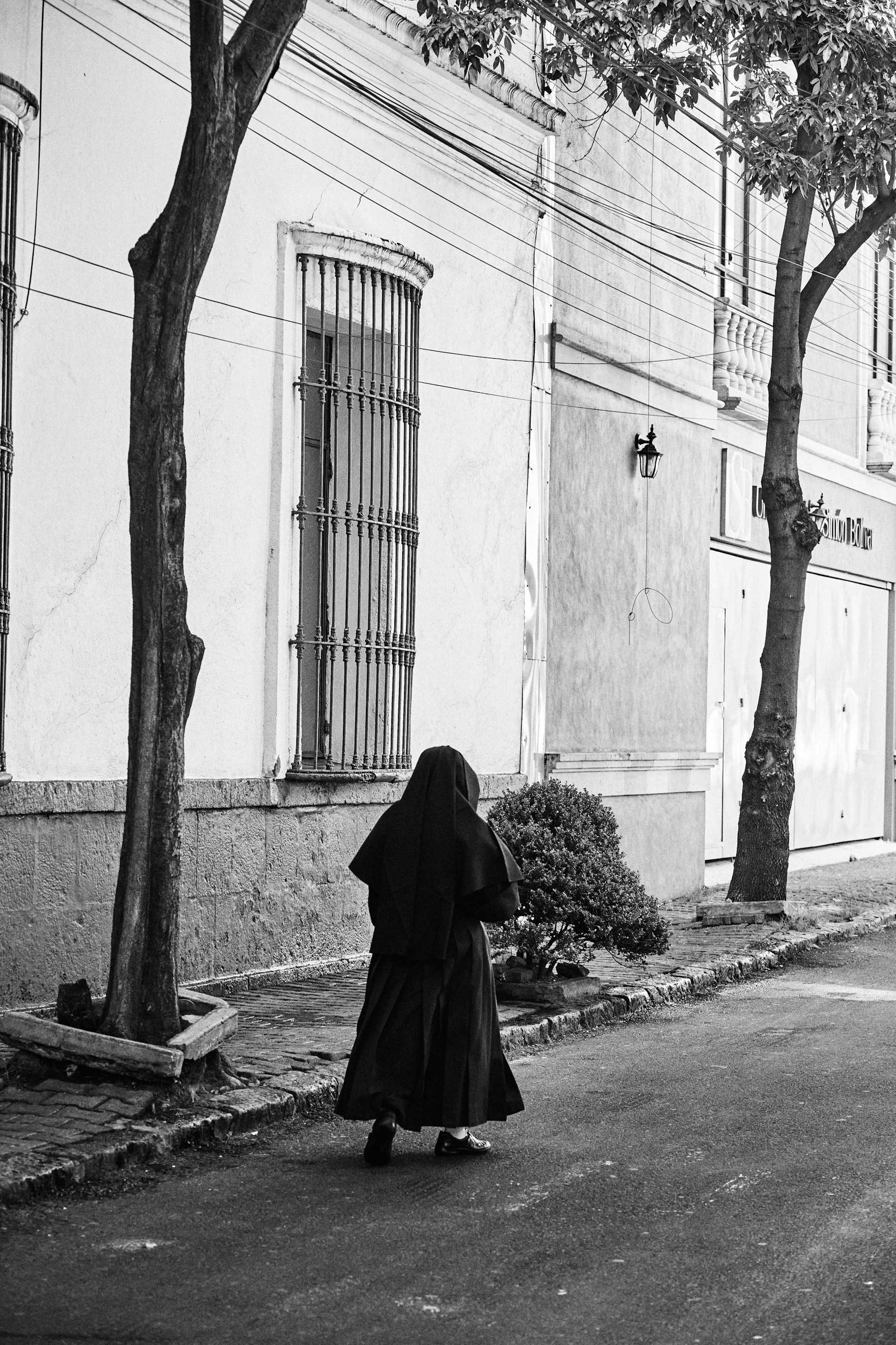 A chic silhouette in the robe Nocturne walking confidently on a cobblestone street, framed by black and white architecture.