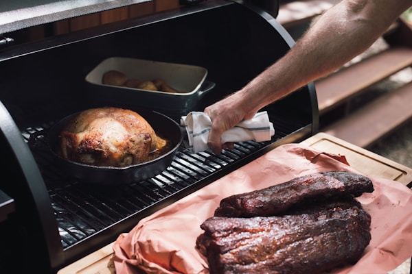 Person holding knife slicing meat on gray metal grill