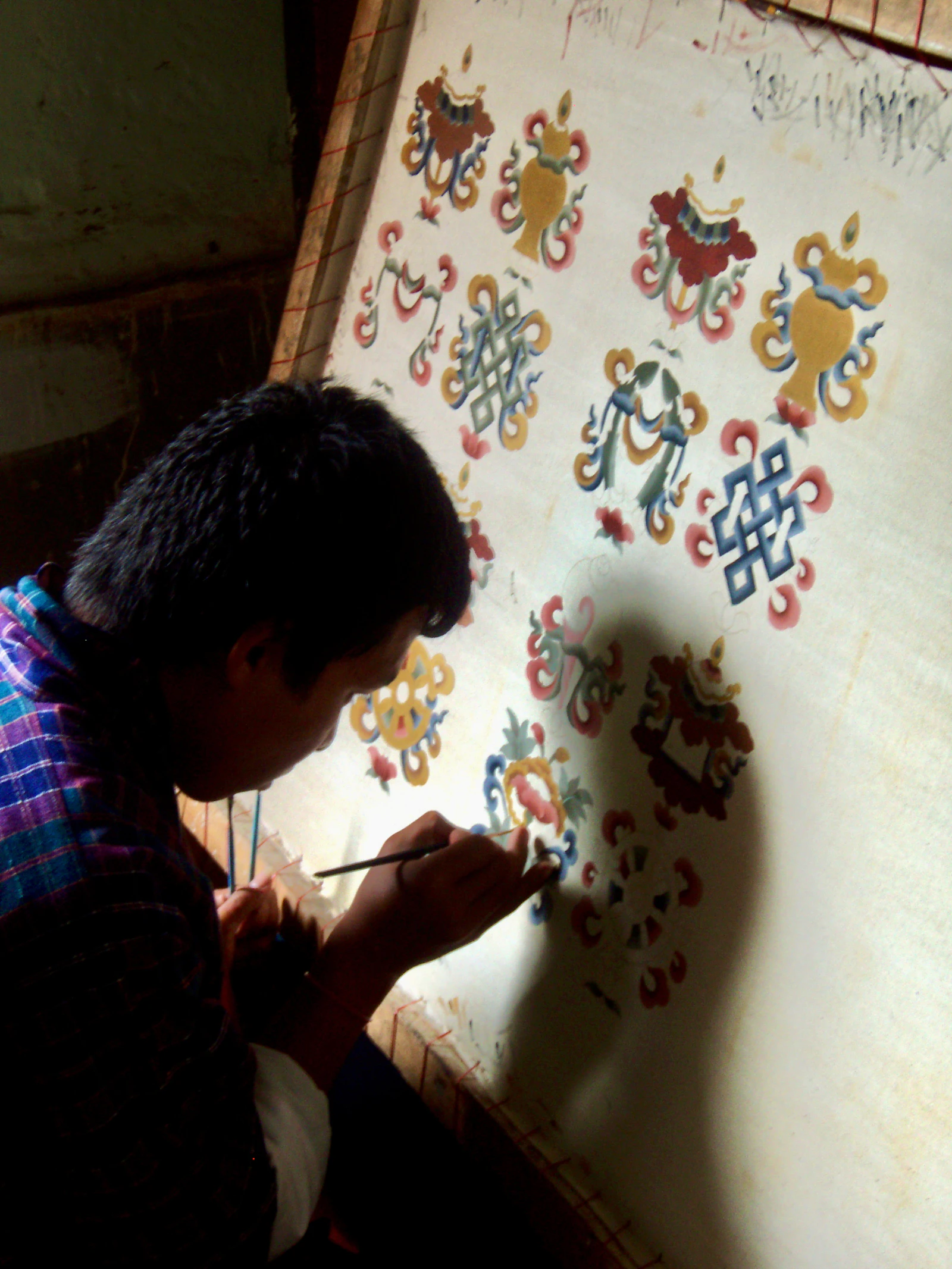 A student painting auspicious symbols on a wall panel at the Choki Traditional Art School in Thimphu