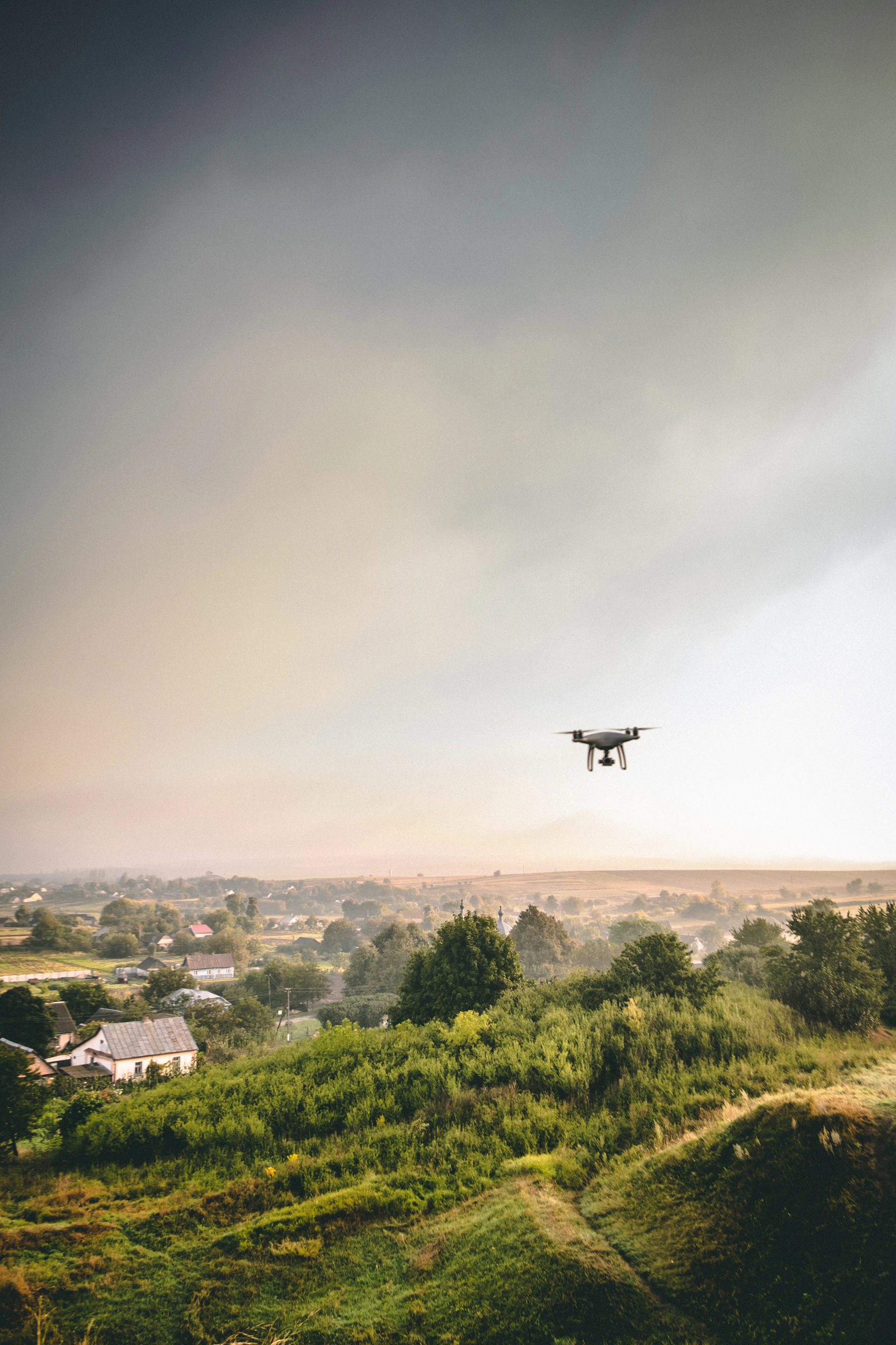 black drone flying over green trees and buildings during daytime