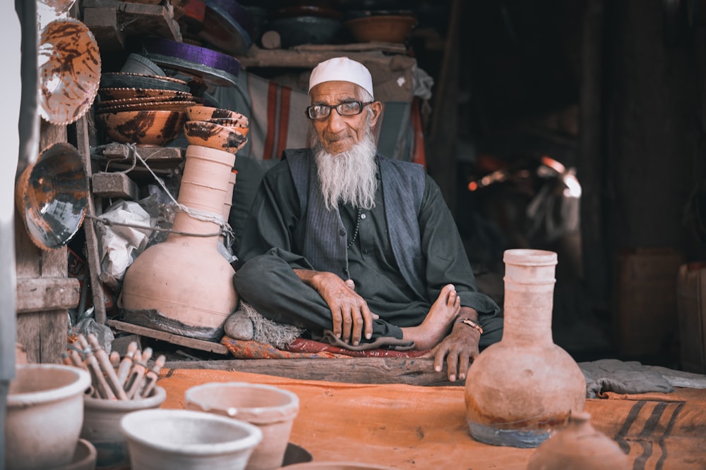 man in gray long sleeve shirt sitting beside brown clay pots