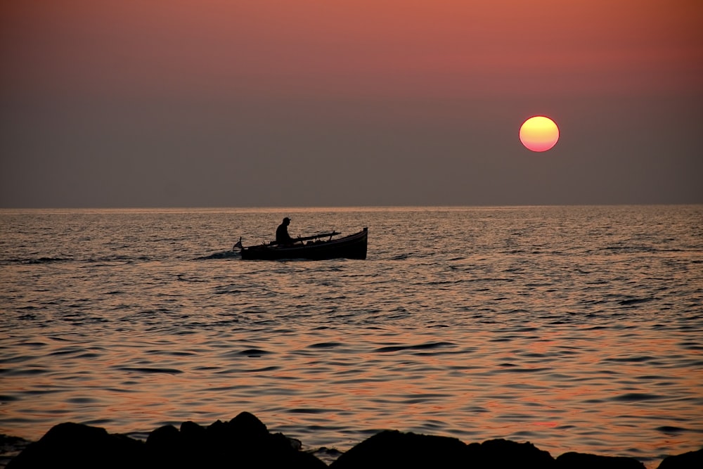 silhouette of man riding on boat during sunset