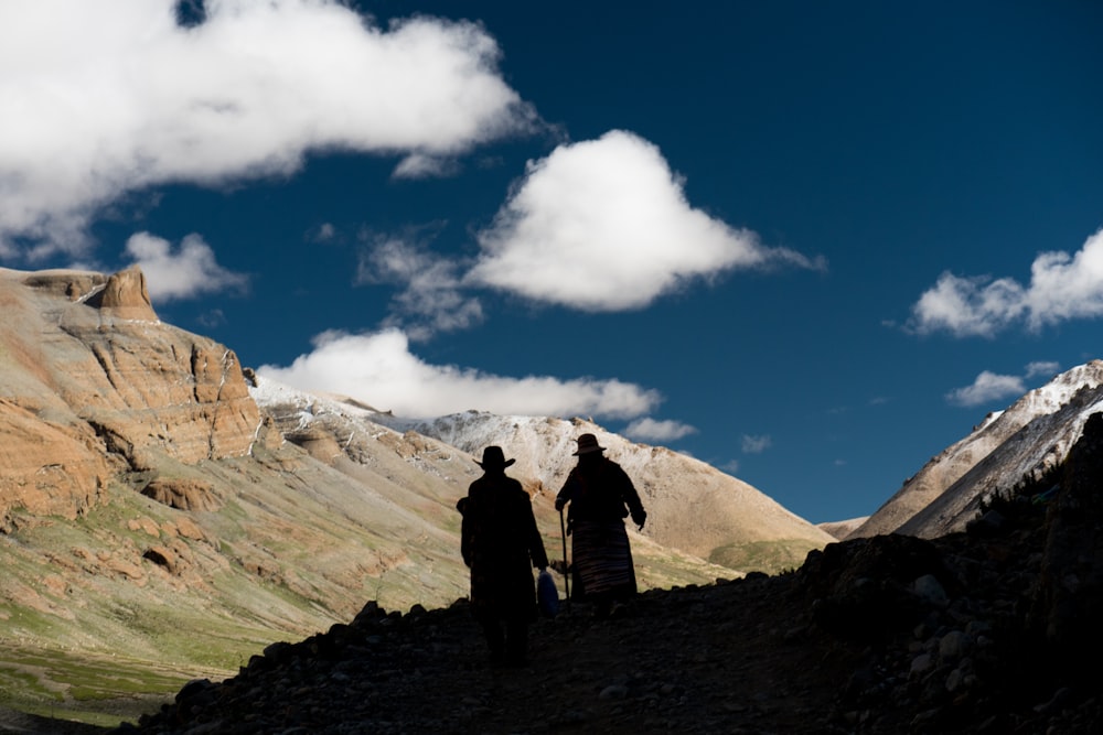 2 person standing on top of mountain under blue sky and white clouds during daytime