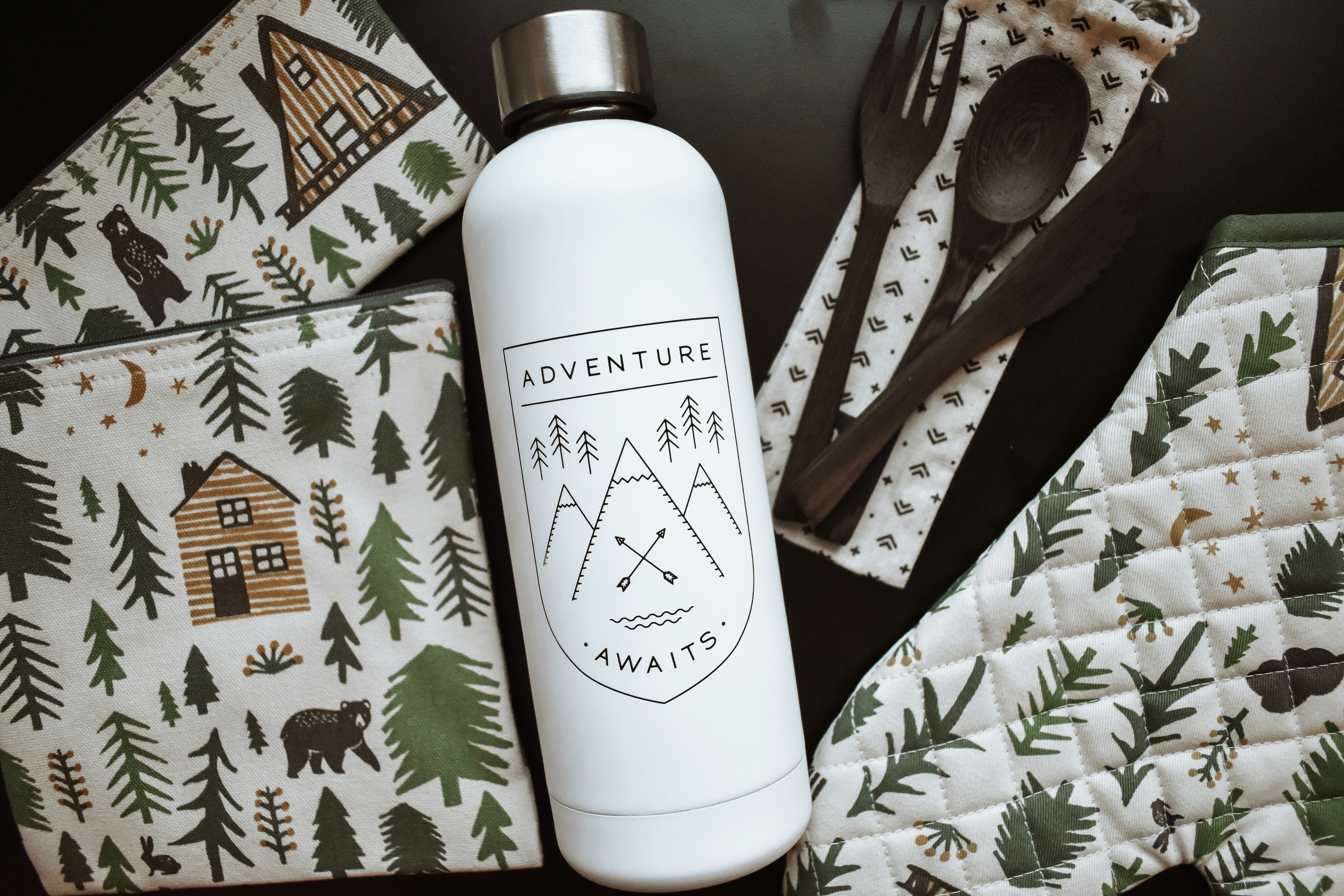 Adventure awaits water bottle flatlay with rustic cabin themed kitchen and camping products and wooden utensils.