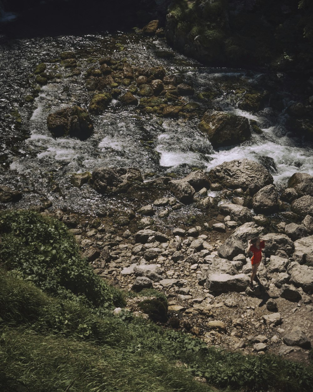 person in red jacket standing on rocky river during daytime