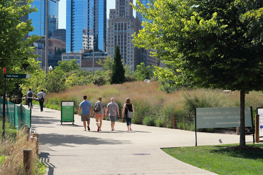 people walking on sidewalk near green trees and high rise buildings during daytime