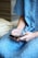 A person wearing a blue hospital gown is seated and using a smartphone. The gown has a checkered pattern with small designs. The focus is on the hands holding the mobile device.