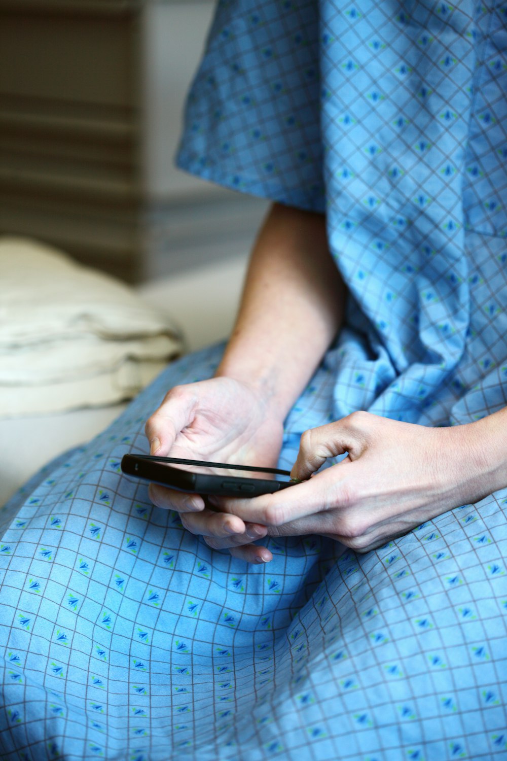 Persona in camicia a scacchi blu e bianchi abbottonata che tiene uno smartphone nero