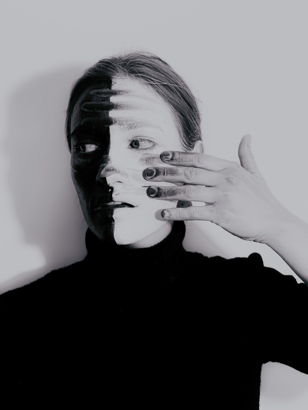 Frau im schwarzen Rollkragenhemd bedeckt ihr Gesicht mit der Hand