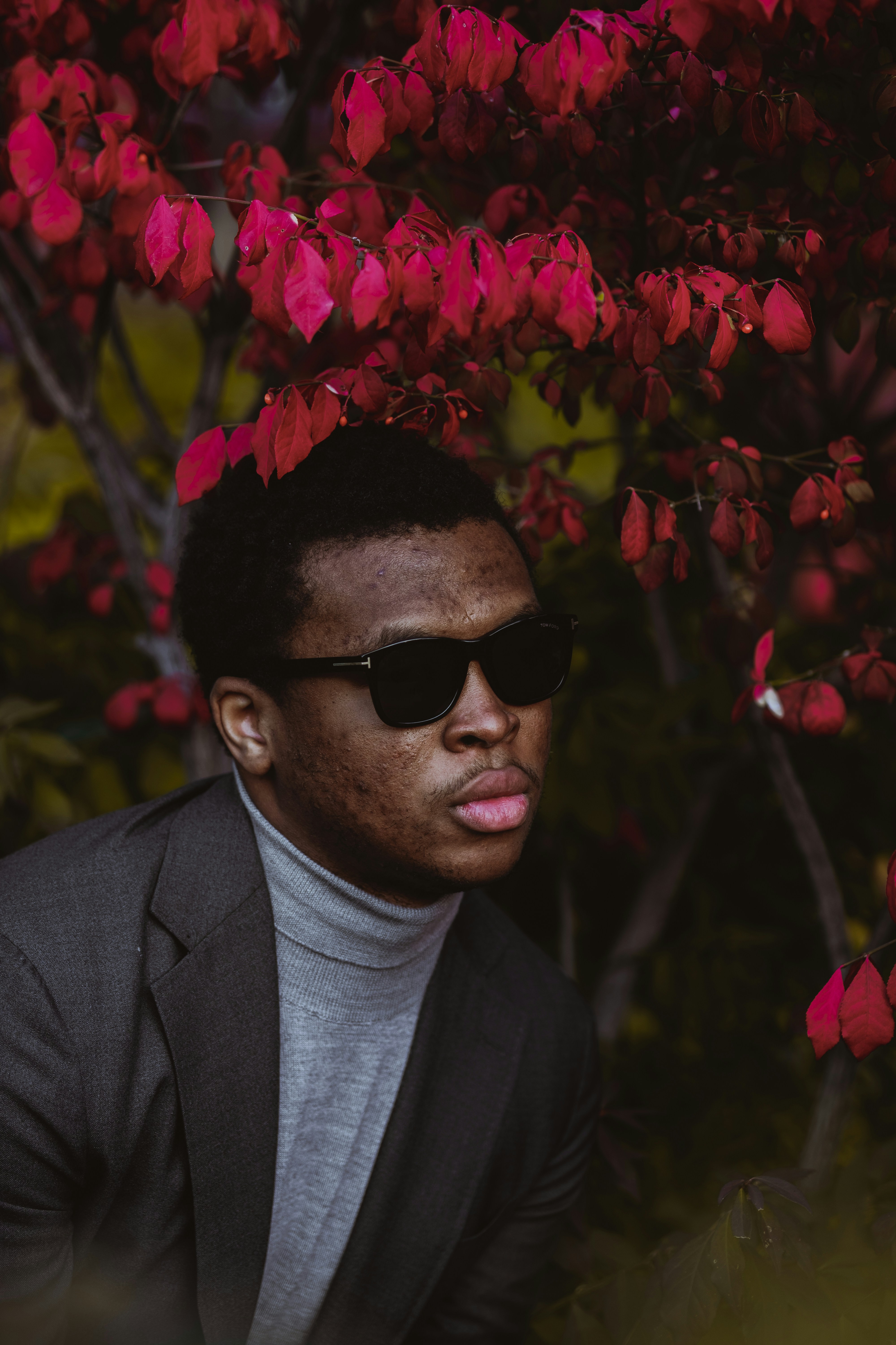 man in black suit wearing black sunglasses standing near pink flowers