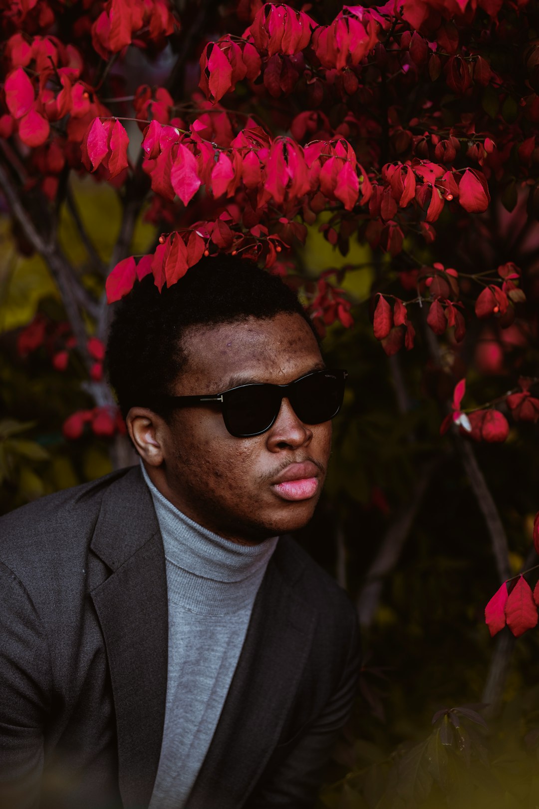 man in black suit wearing black sunglasses standing near pink flowers