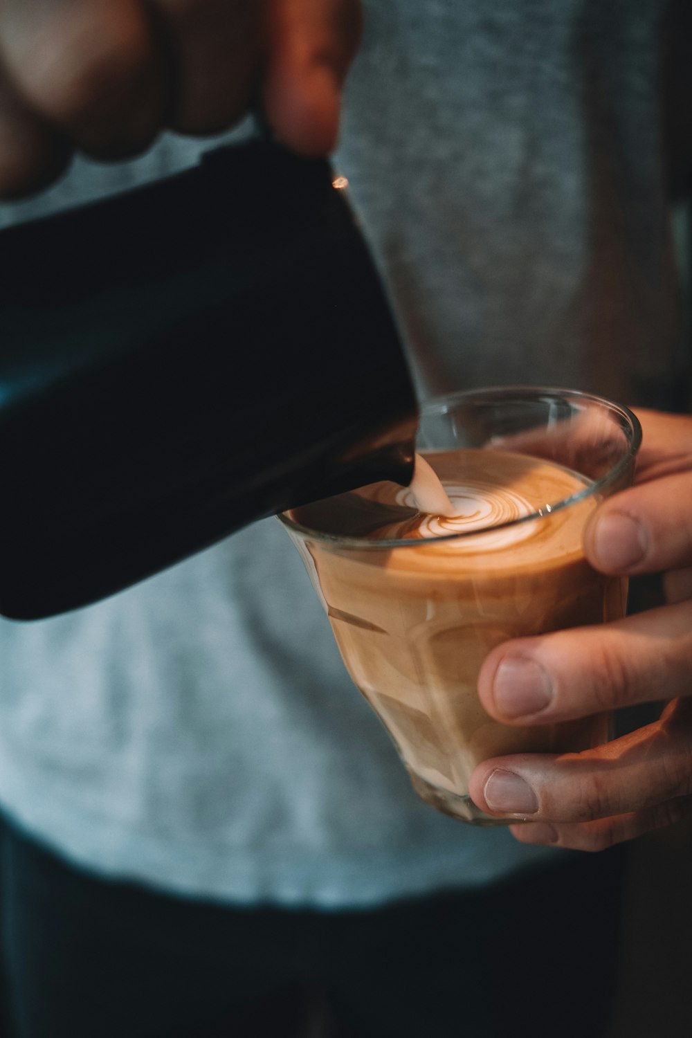 person pouring brown liquid on clear drinking glass