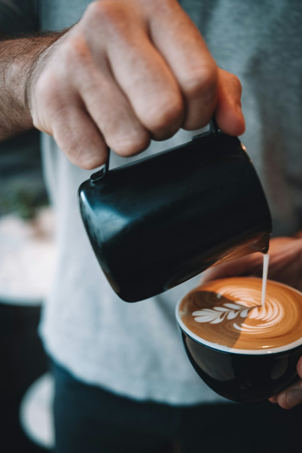 personne versant du café sur une tasse en céramique noire