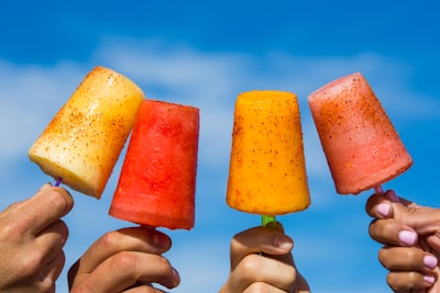 Smiling hands holding a variety of long ice pops against a bright blue sky.