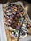 A rectangular waffle topped with whipped cream, colorful chocolate candies, chocolate syrup, and pieces of chocolate bar is displayed. The waffle is sprinkled with powdered sugar and served on a white plastic tray.