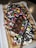 A rectangular waffle topped with whipped cream, colorful chocolate candies, chocolate syrup, and pieces of chocolate bar is displayed. The waffle is sprinkled with powdered sugar and served on a white plastic tray.