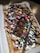 A rectangular waffle topped with whipped cream, colorful chocolate candies, chocolate syrup, and pieces of chocolate bar is displayed. The waffle is sprinkled with powdered sugar and served on a white plastic tray.