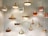 A collection of hanging pendant lights with varied shapes and sizes, featuring metallic finishes in gold and brass tones. They are suspended from the ceiling against a plain, softly lit background.