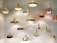 A collection of hanging pendant lights with varied shapes and sizes, featuring metallic finishes in gold and brass tones. They are suspended from the ceiling against a plain, softly lit background.