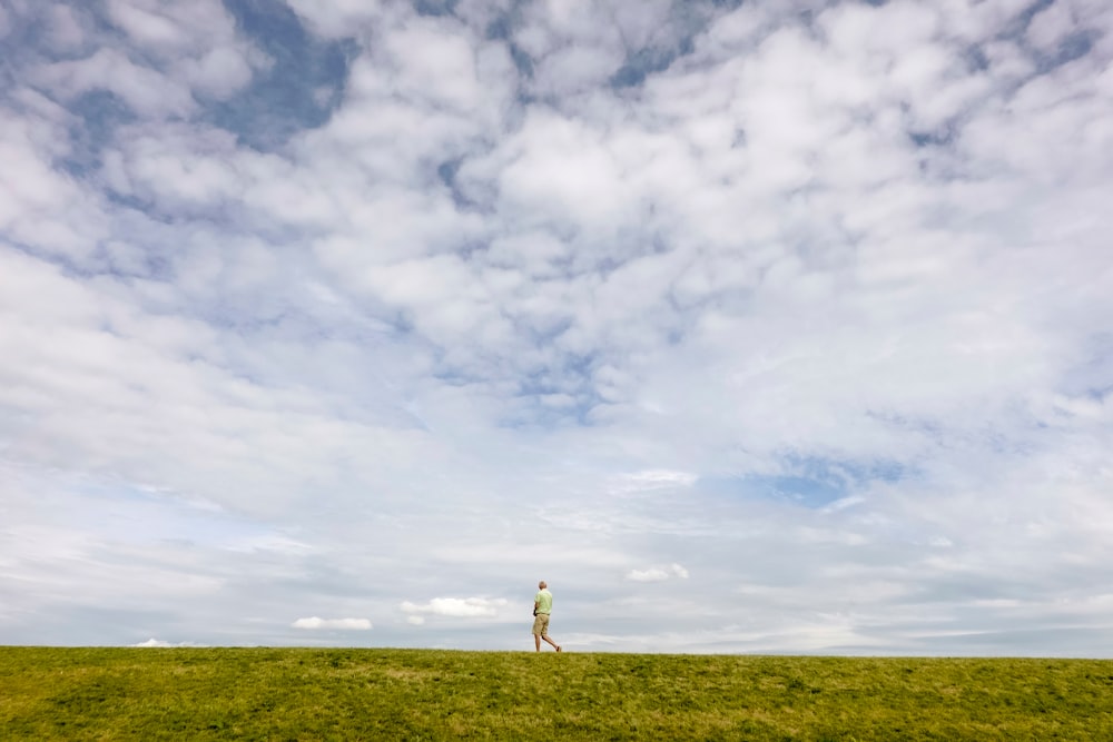 person standing on green grass field under white clouds and blue sky during daytime