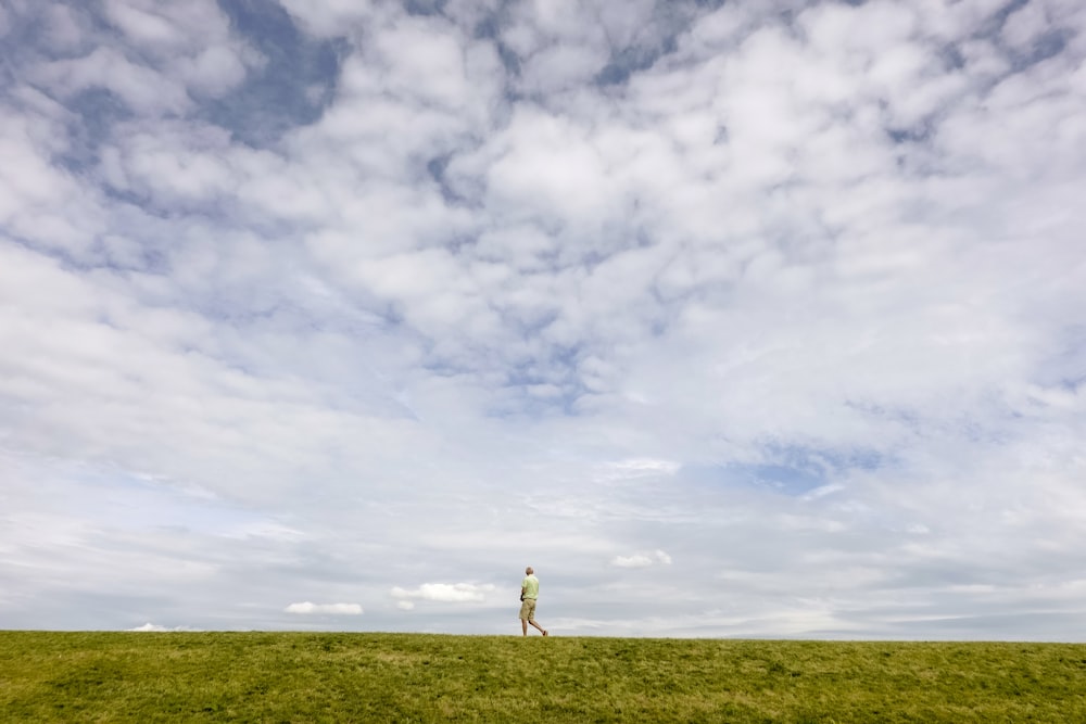 person standing on green grass field under white clouds and blue sky during daytime