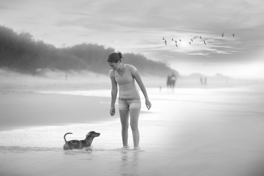 Frau im weißen Bikini geht mit Hund am Strand spazieren
