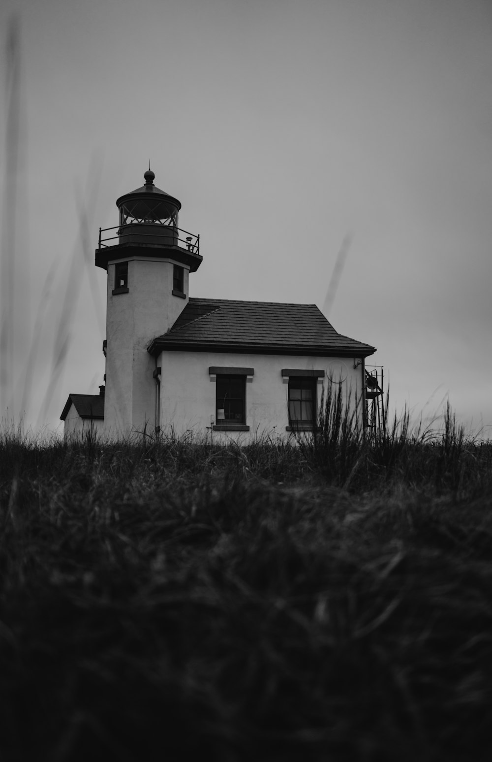 Foto en escala de grises del faro cerca de un campo de hierba