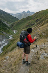 man in black and red backpack and black backpack standing on green grass field during daytime