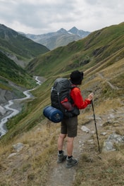 man in black and red backpack and black backpack standing on green grass field during daytime