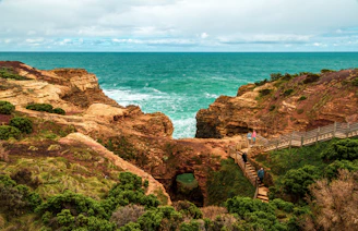 A sunlit coastal trail winding along rugged cliffs with turquoise ocean waves crashing below.