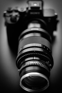 Black and white photo of a film camera lens with subtle reflections, emphasizing precision and focus.