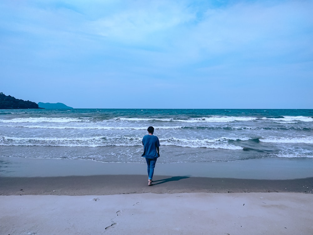 woman in blue jacket walking on beach during daytime