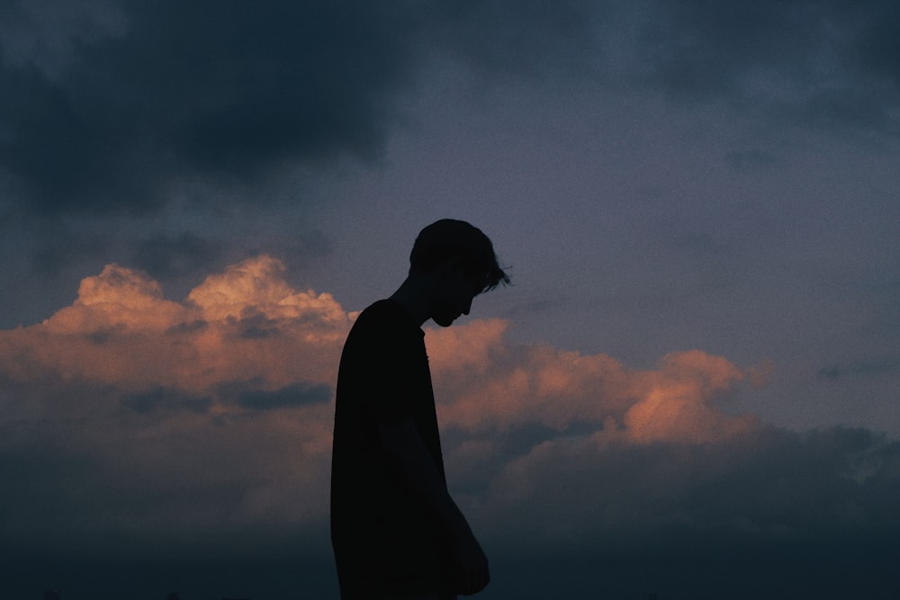 silhouette of man standing under cloudy sky during daytime