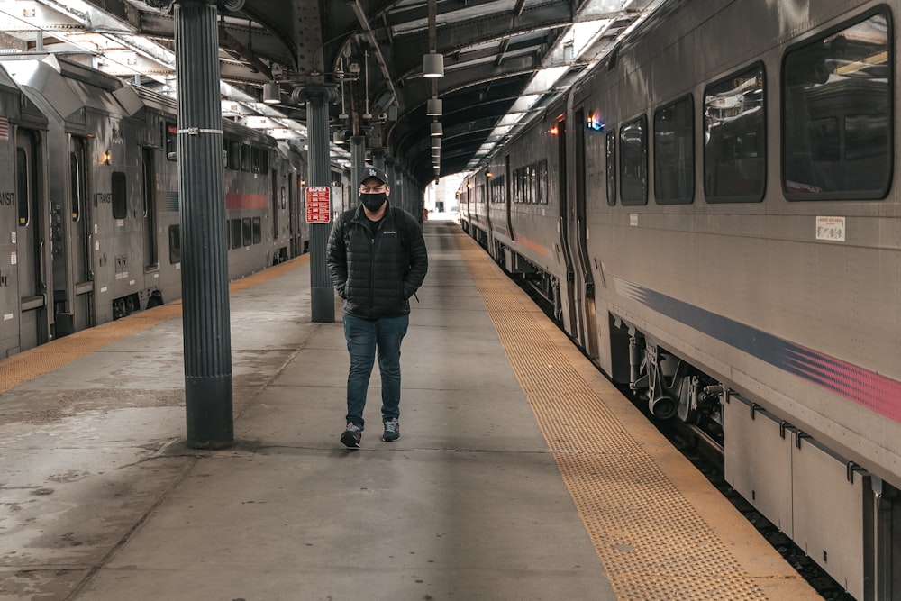 man in black jacket and blue denim jeans standing on train station