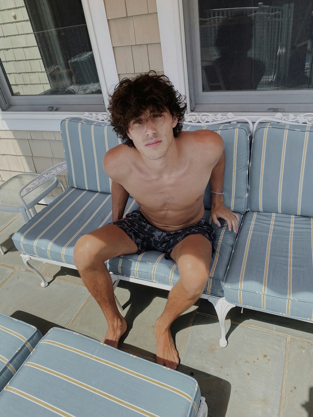 topless man sitting on white and blue striped armchair