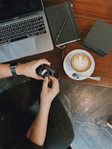 A person analyzing tech gadgets on a desk with a notebook and coffee cup.