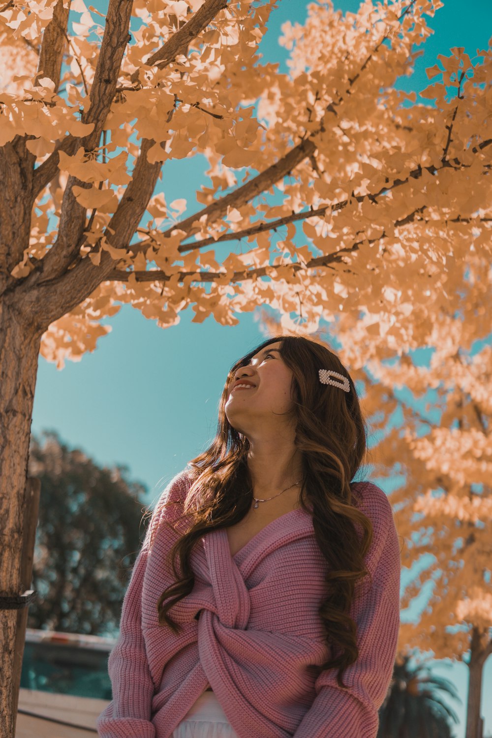 woman in pink knit sweater standing under brown tree during daytime