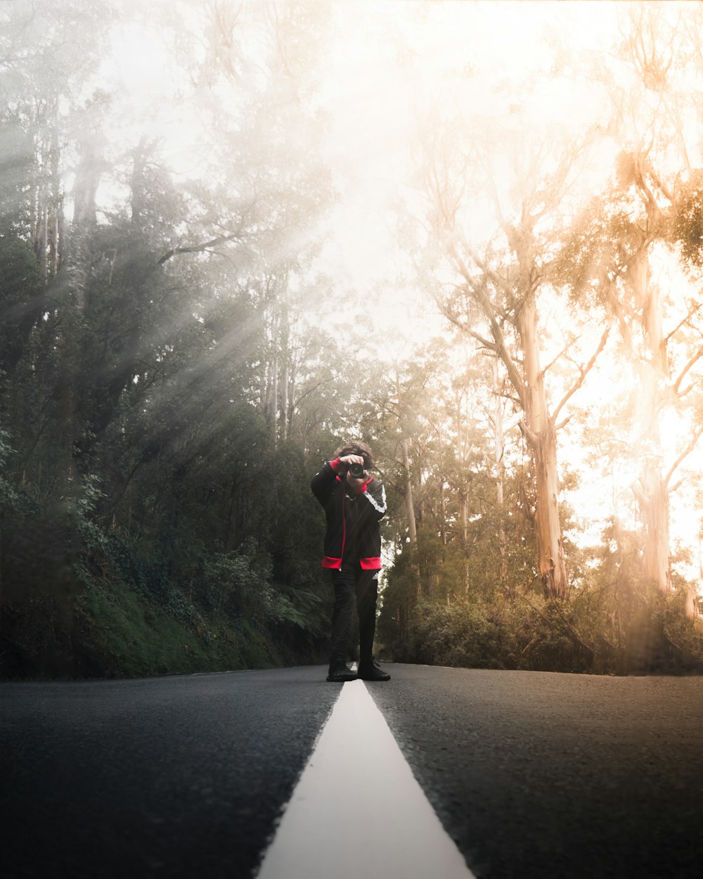 person in black jacket and black pants standing on road between trees during daytime