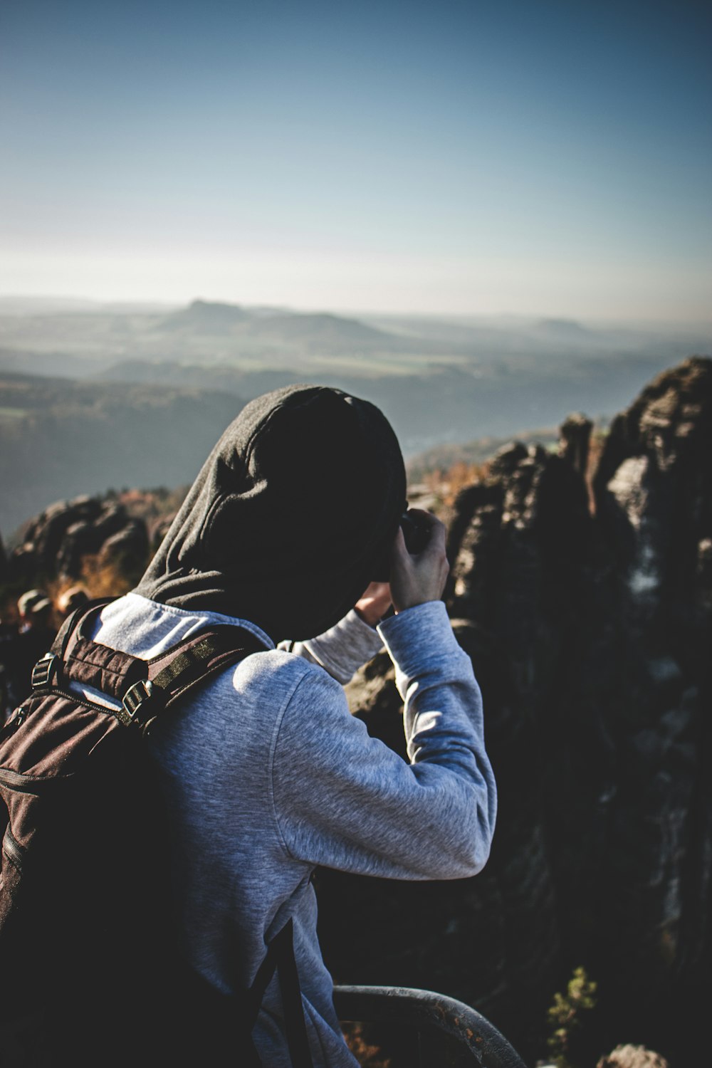 person in gray hoodie and black backpack standing on cliff during daytime