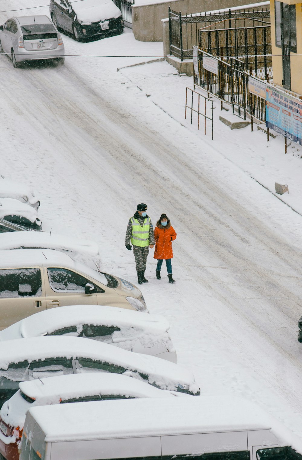uomo in giacca arancione che cammina sulla strada coperta di neve durante il giorno