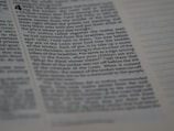 A close-up of text from a book with a biblical or religious theme. The text appears formatted in columns and includes chapter and verse numbers. The page is in focus on the left and gradually blurs toward the right edge.
