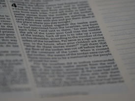 A close-up of text from a book with a biblical or religious theme. The text appears formatted in columns and includes chapter and verse numbers. The page is in focus on the left and gradually blurs toward the right edge.