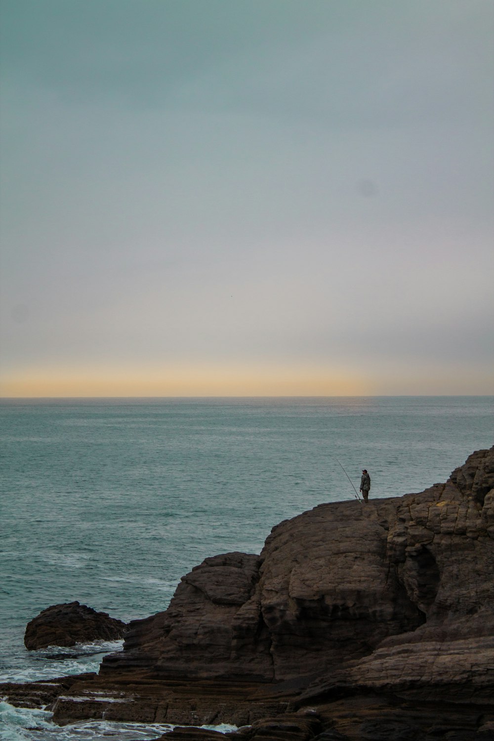 person standing on rock formation near body of water during daytime