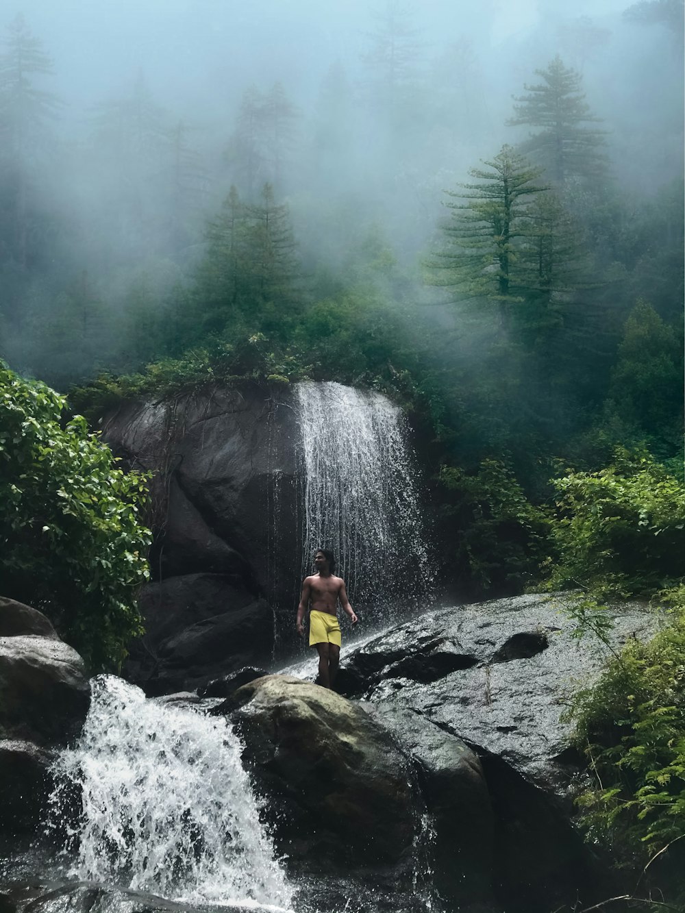 woman in yellow jacket sitting on rock near waterfalls during daytime