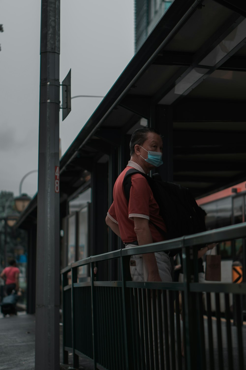 man in black jacket and orange jacket standing near black metal railings during daytime