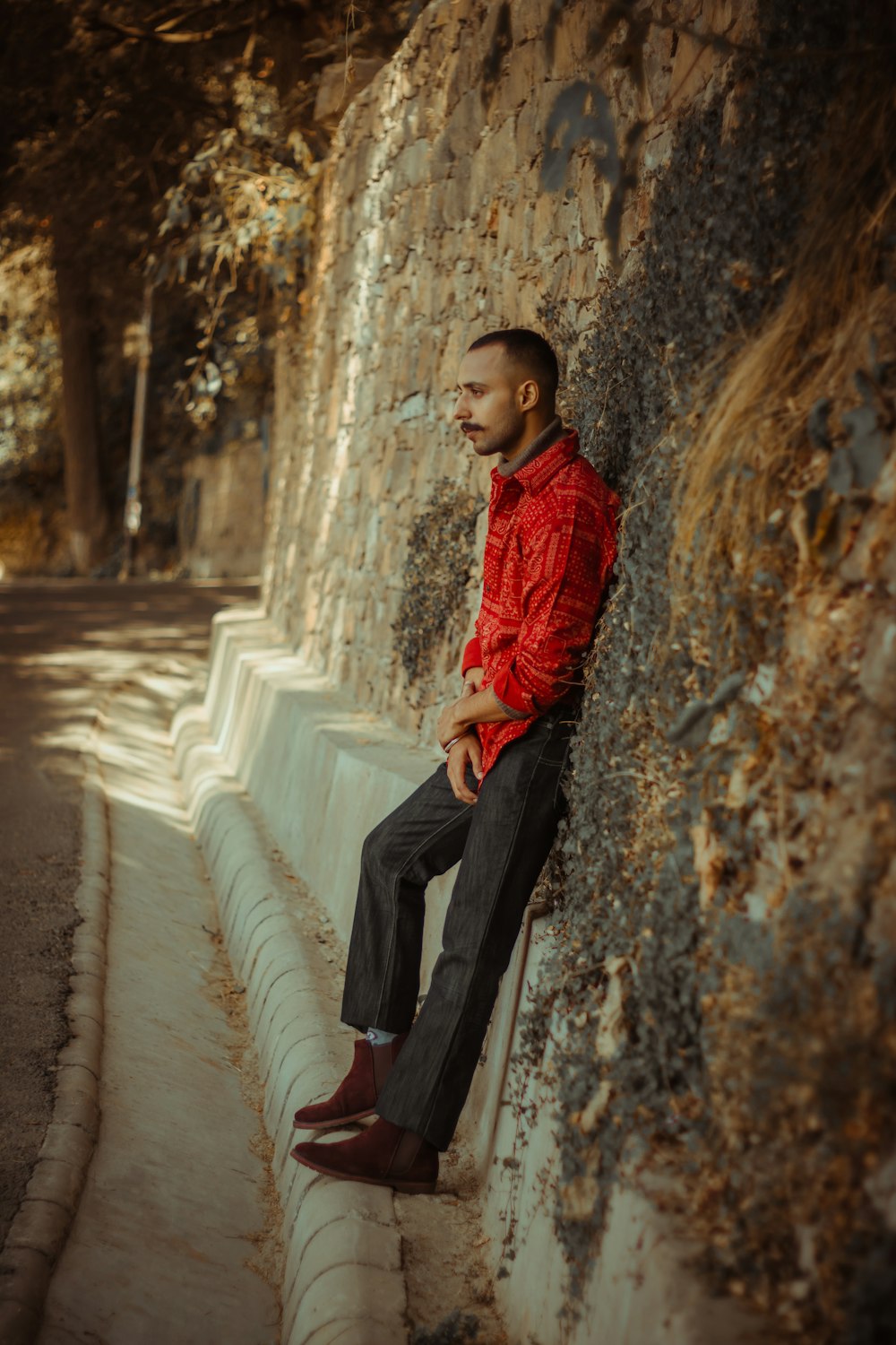boy in red jacket and black pants sitting on concrete wall during daytime