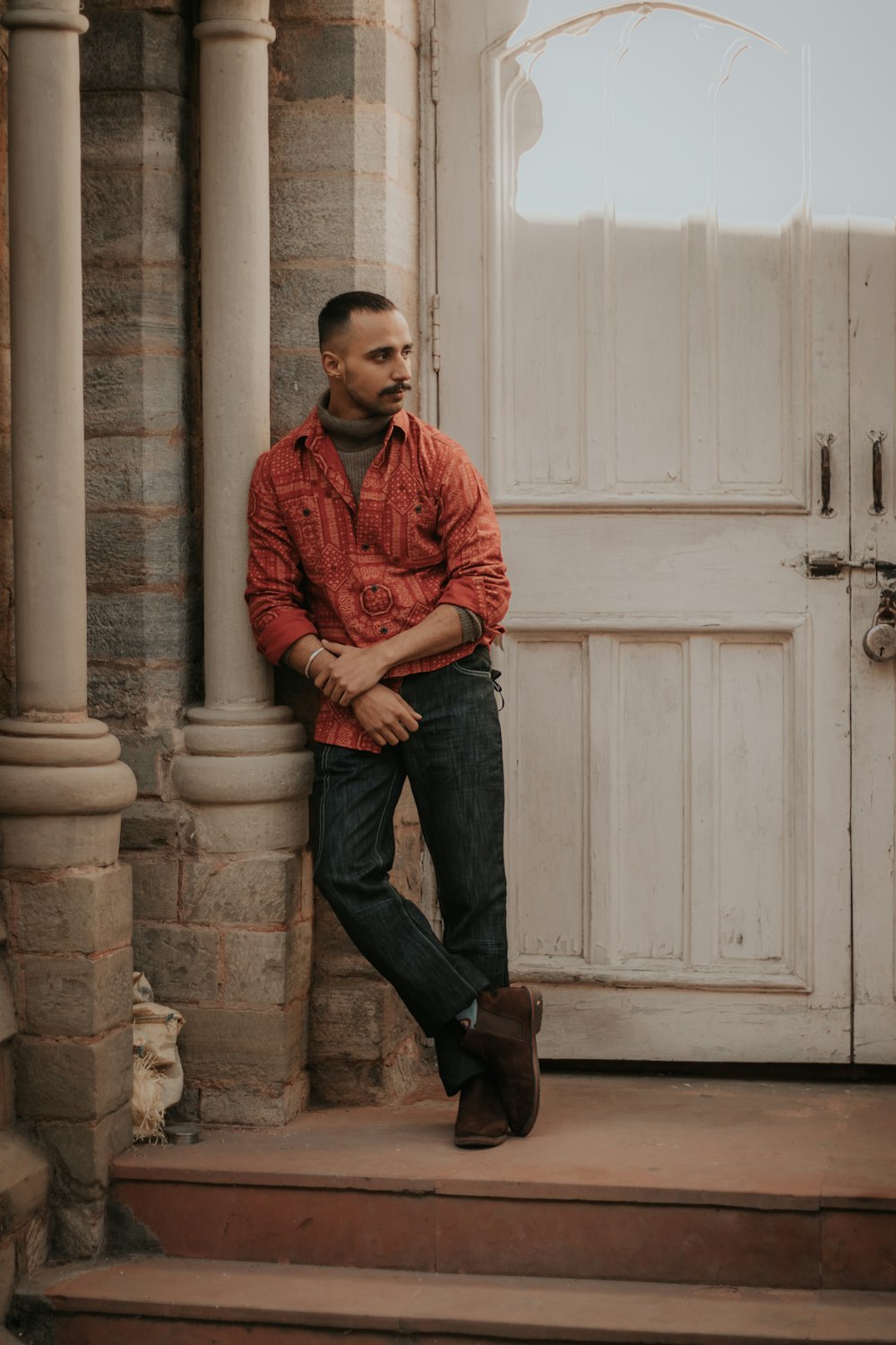 man in red and blue plaid dress shirt and blue denim jeans sitting on brown concrete