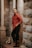 man in red dress shirt and black denim jeans sitting on concrete column