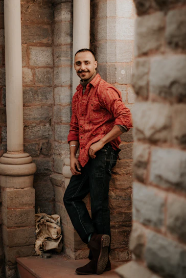 A casually dressed man wearing a soft cotton t-shirt standing against a rustic brick wall.